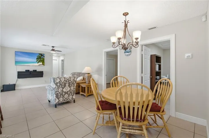Open-concept living and dining area featuring neutral tile flooring, a multi-light chandelier, and ceiling fan