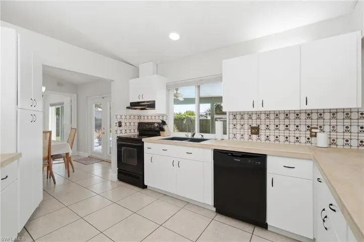 Kitchen featuring white cabinetry with dark hardware, black appliances, light-toned countertops, and a patterned tile backsplash