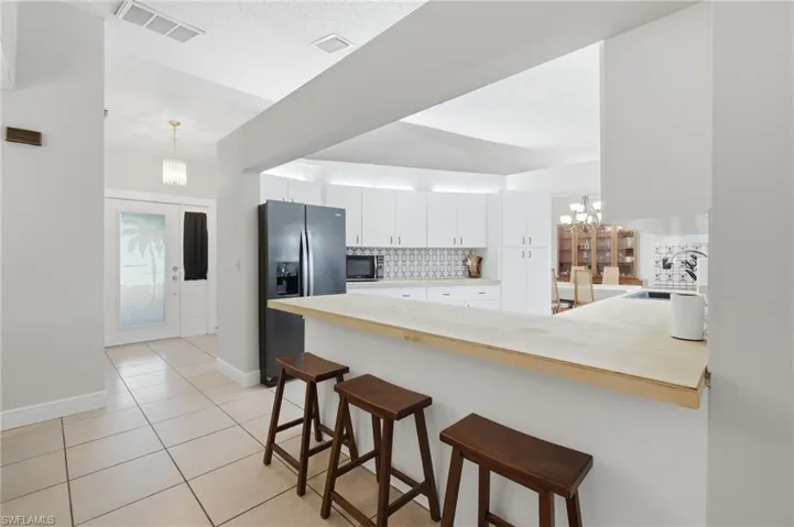 Open kitchen with light wood-finish breakfast bar, white cabinetry, and modern tile backsplash