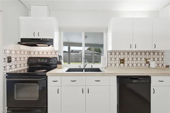 Kitchen featuring white cabinetry, black appliances, a black double-basin sink, and light wood-finish countertops