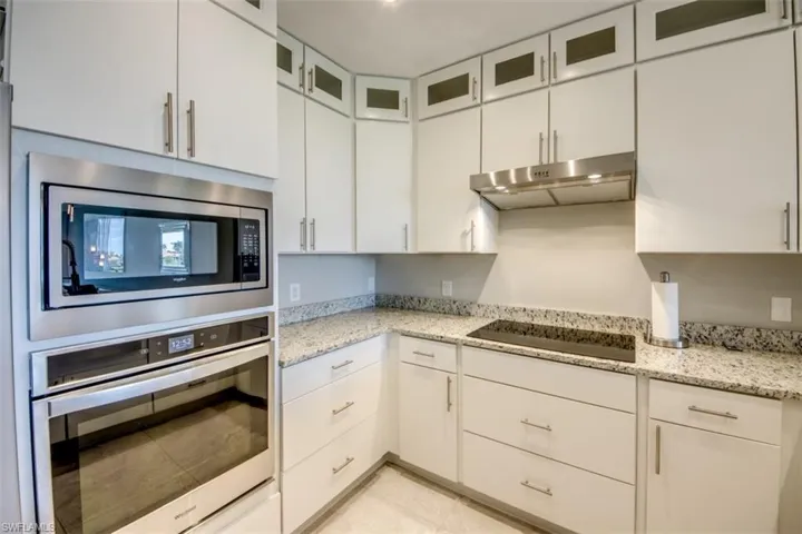 Kitchen featuring under cabinet range hood, light stone countertops, glass insert cabinets, and appliances with stainless steel finishes