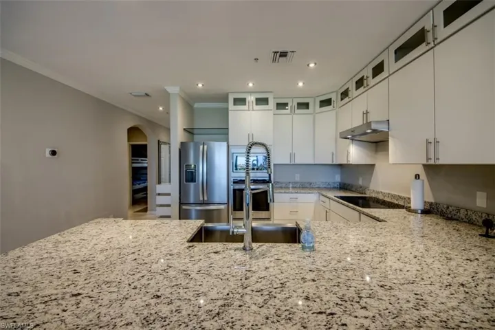 Kitchen featuring light stone countertops, arched walkways, ornamental molding, visible vents, and stainless steel appliances