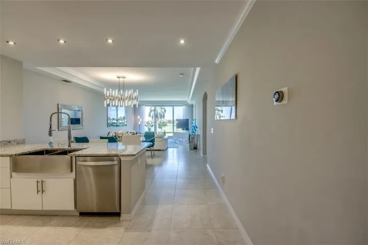 Kitchen featuring light stone countertops, ornamental molding, a chandelier, dishwasher, and a sink