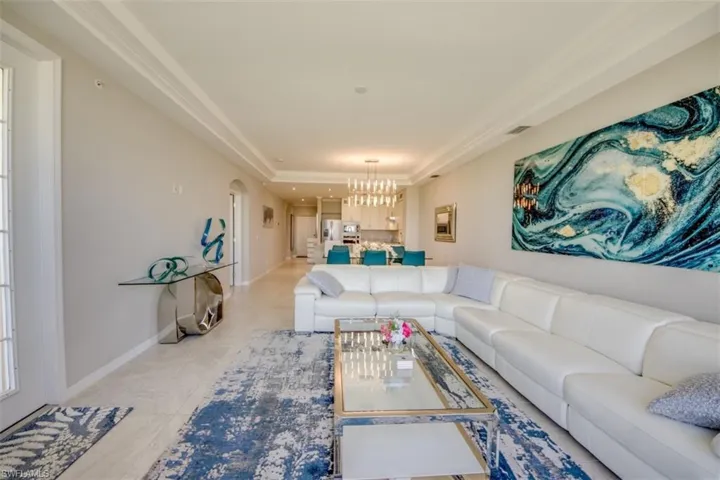 Living room with a notable chandelier, baseboards, visible vents, a raised ceiling, and arched walkways