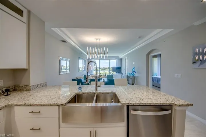 Kitchen featuring a sink, stainless steel dishwasher, white cabinetry, and light stone countertops