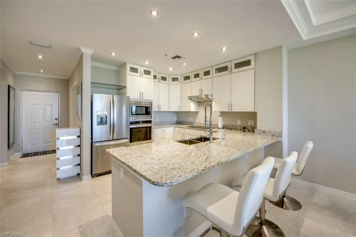 Kitchen featuring a peninsula, under cabinet range hood, crown molding, light stone countertops, and stainless steel appliances