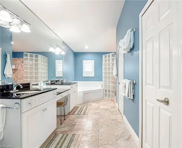 Bathroom featuring a bath, double vanity, light marble finish floors, and recessed lighting