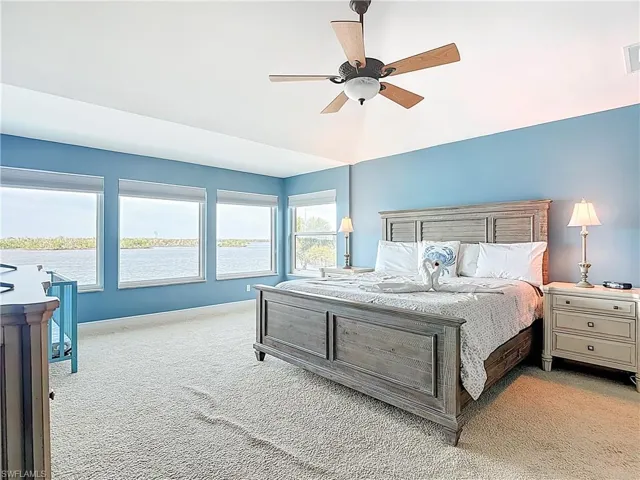 Bedroom with light colored carpet, ceiling fan, and a water view