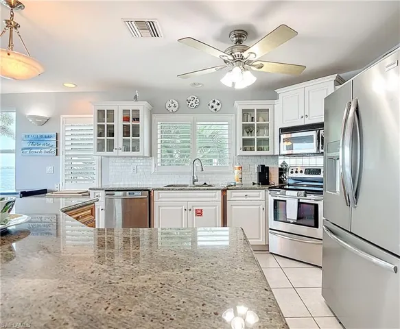 Kitchen featuring appliances with stainless steel finishes, glass insert cabinets, light stone countertops, white cabinets, and decorative backsplash