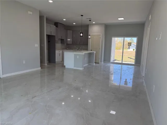 Kitchen featuring open floor plan, an island with sink, hanging light fixtures, light marble finish floors, and a kitchen bar