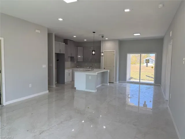 Kitchen featuring open floor plan, a center island with sink, light marble finish flooring, hanging light fixtures, and light stone countertops