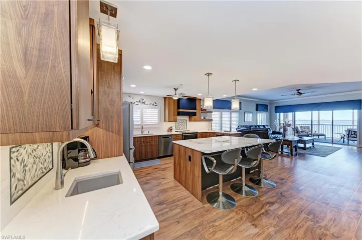 Kitchen with wood finish cabinets, open floor plan, ceiling fan, light stone countertops, and dark wood-type flooring