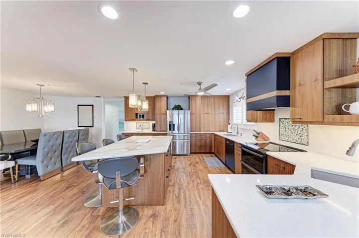 Kitchen featuring wood finish cabinetry, open shelves, stainless steel fridge with ice dispenser, light wood-style flooring, and range with two ovens