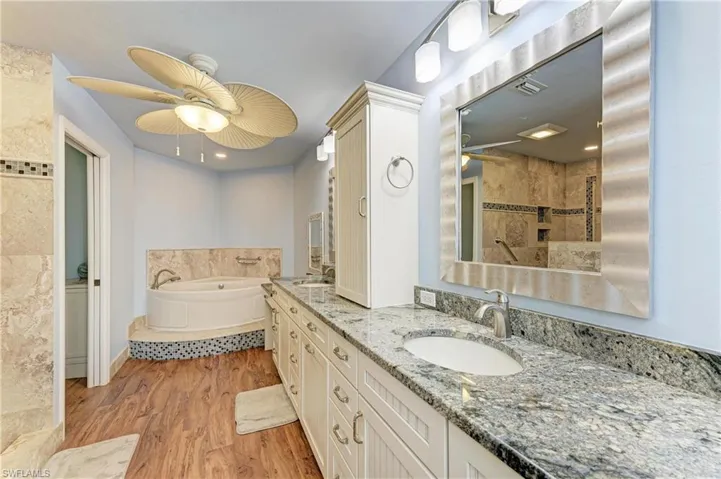Bathroom featuring a garden tub, double vanity, light wood-style flooring, a ceiling fan, and a tile shower