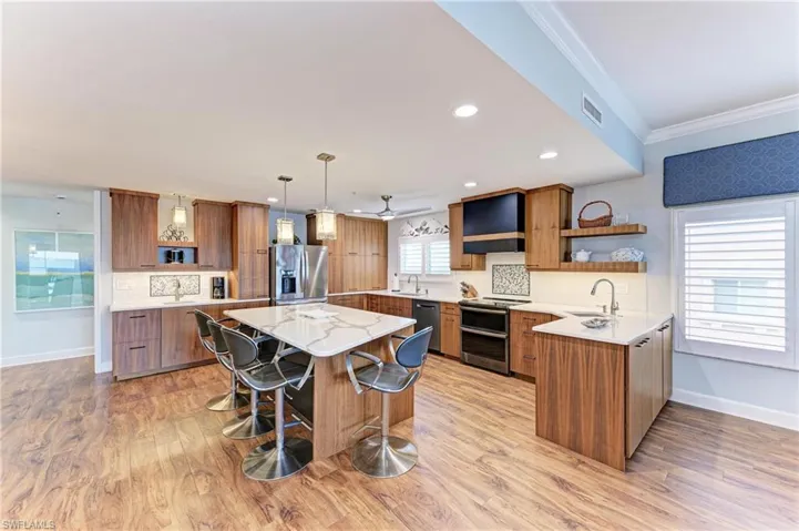 Kitchen with open shelves, light stone counters, wood finish cabinets, a breakfast bar, and crown molding