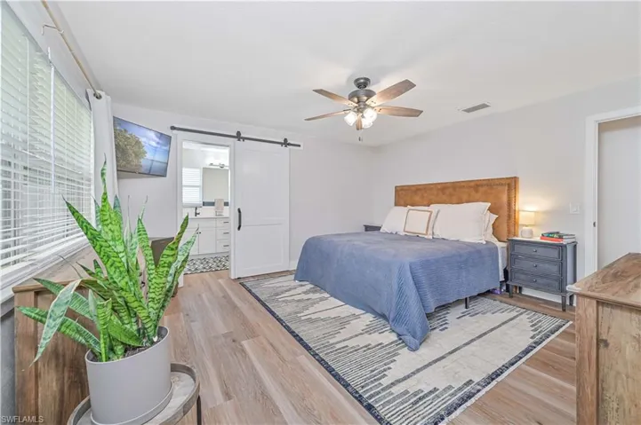 Bedroom with light hardwood / wood-style flooring, a barn door, and ceiling fan