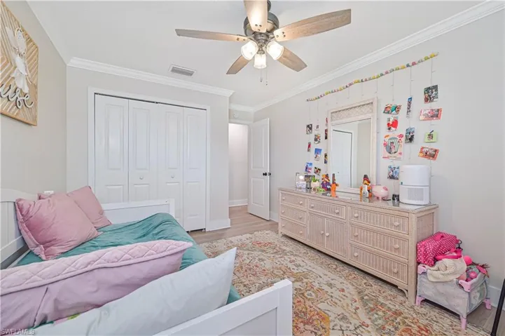 Bedroom with ceiling fan, a closet, light wood-type flooring, and ornamental molding