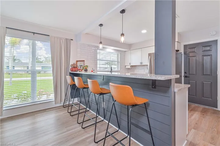 Kitchen with kitchen peninsula, hanging light fixtures, a breakfast bar area, backsplash, and white cabinetry