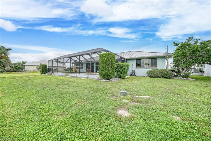 Rear view of property featuring glass enclosure, a sunroom, and a lawn