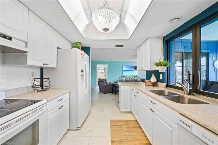 Kitchen featuring white appliances, white cabinetry, light stone countertops, and a chandelier