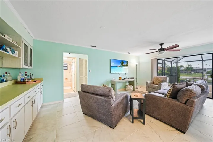 Living room with a ceiling fan, ornamental molding, light tile patterned flooring, and a textured ceiling