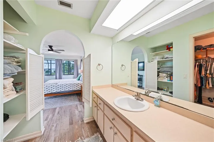 Bathroom with vanity, light wood finished floors, a spacious closet, ensuite bathroom, and ceiling fan