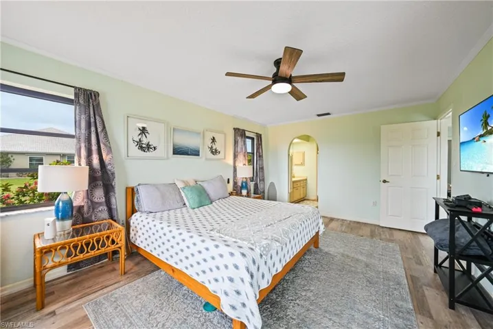 Bedroom with ensuite bath, multiple windows, wood finished floors, and crown molding