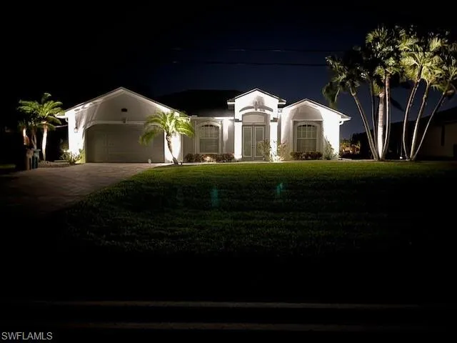 View of front of property with decorative driveway, a garage, and a lawn