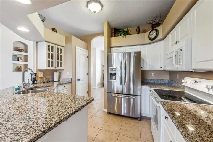 Kitchen with a sink, white cabinetry, glass insert cabinets, light tile patterned floors, and white appliances