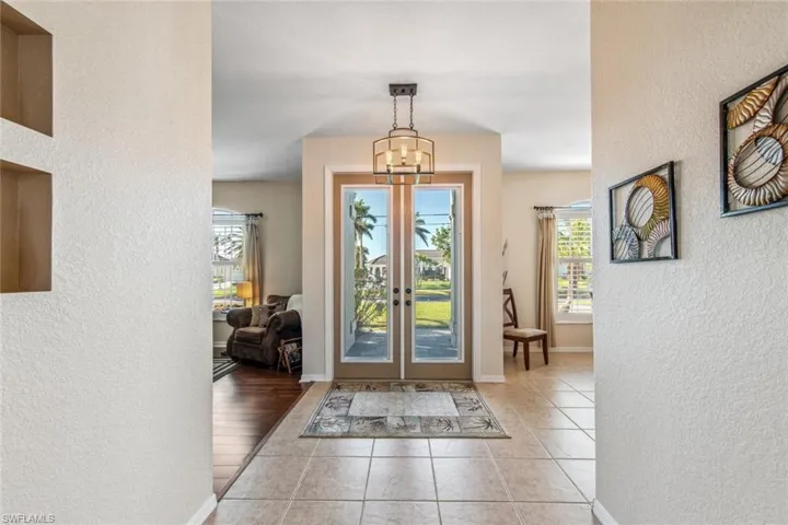Foyer entrance with light tile patterned flooring, baseboards, a textured wall, french doors, and a notable chandelier