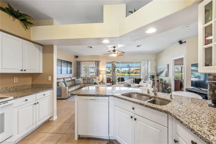 Kitchen with white appliances, light stone counters, a ceiling fan, a sink, and open floor plan