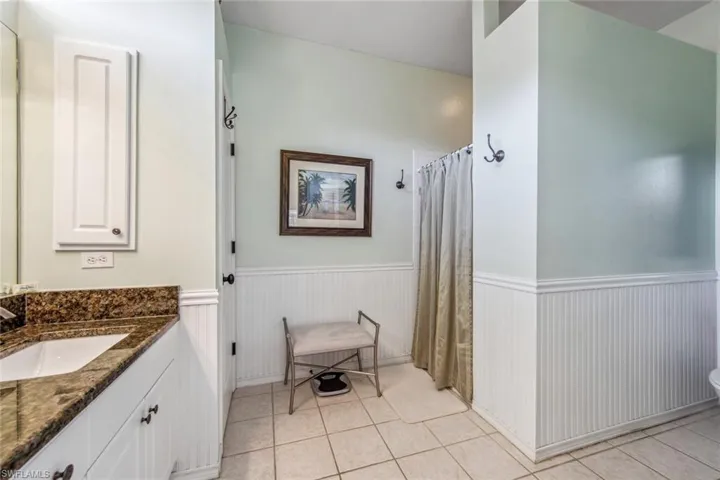 Full bathroom with tile patterned floors, wainscoting, curtained shower, and vanity