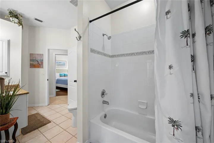 Ensuite bathroom with shower / bath combo with shower curtain, visible vents, tile patterned floors, and toilet