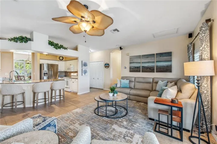 Living area featuring light tile patterned floors, baseboards, visible vents, arched walkways, and ceiling fan
