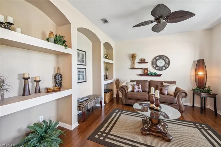 Living room featuring a ceiling fan, visible vents, built in shelves, and wood finished floors