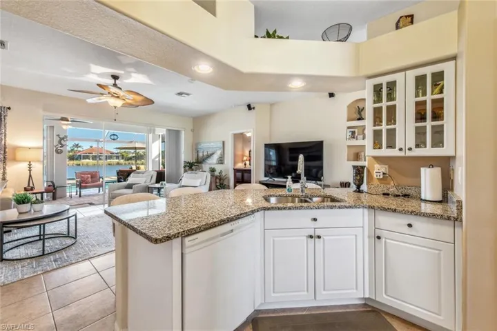 Kitchen with a peninsula, dishwasher, light stone counters, a sink, and open floor plan
