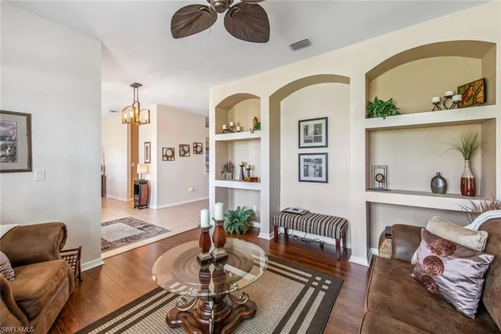 Living area with built in features, wood finished floors, ceiling fan with notable chandelier, and visible vents