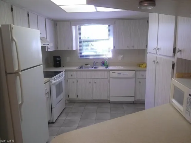 Kitchen with sink, white appliances, light tile floors, and tasteful backsplash
