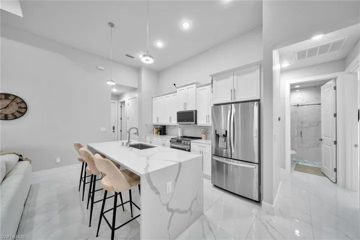 Kitchen featuring sink, appliances with stainless steel finishes, white cabinetry, light stone countertops, and a center island with sink