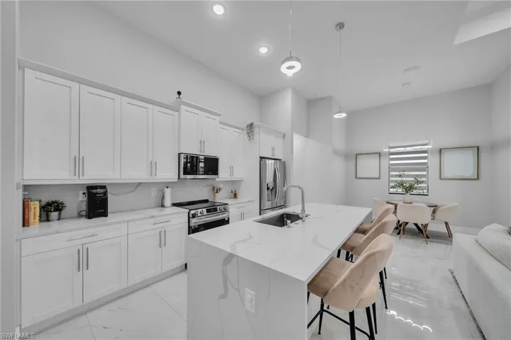 Kitchen featuring sink, decorative light fixtures, stainless steel appliances, light stone countertops, and white cabinets