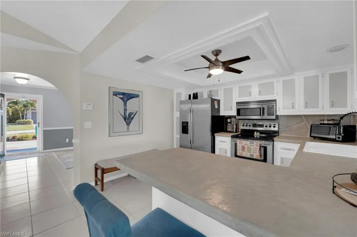 Kitchen featuring stainless steel appliances, arched walkways, a raised ceiling, a peninsula, and ceiling fan