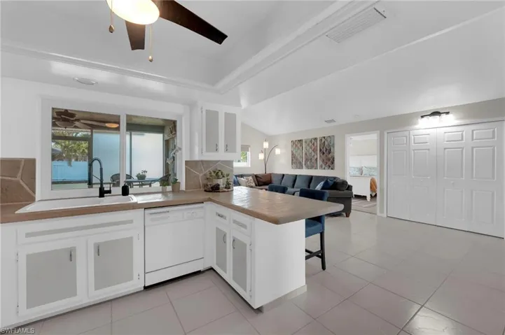 Kitchen with a ceiling fan, white dishwasher, white cabinets, backsplash, and a peninsula