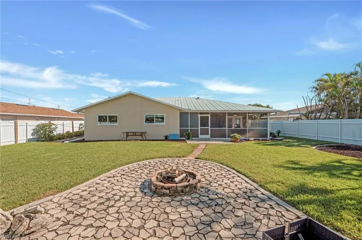 Back of house with stucco siding, a sunroom, a fenced backyard, an outdoor fire pit, and a patio area