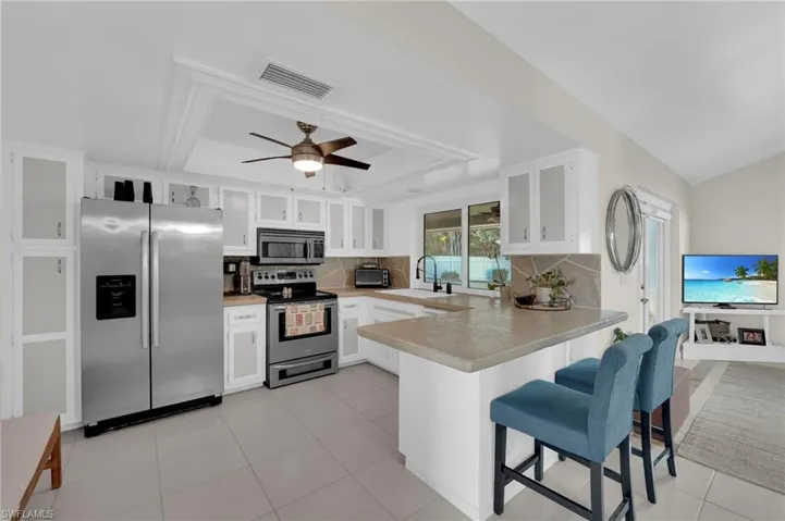 Kitchen with stainless steel appliances, a peninsula, a raised ceiling, decorative backsplash, and light countertops