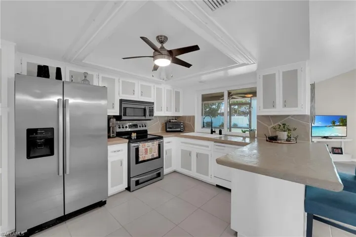 Kitchen with a peninsula, appliances with stainless steel finishes, tasteful backsplash, and a ceiling fan