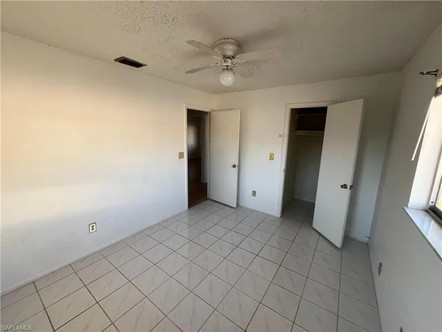 Unfurnished bedroom with a textured ceiling, a ceiling fan, a spacious closet, and light tile patterned floors
