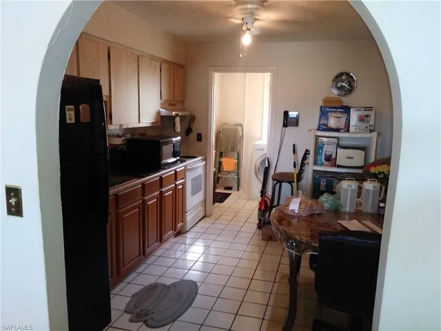 Kitchen with arched walkways, black appliances, light tile patterned floors, and washer / clothes dryer