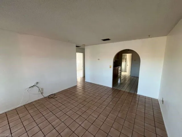 Tiled empty room featuring arched walkways and a textured ceiling