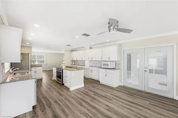 Kitchen featuring hardwood / wood-style floors, white cabinets, ornamental molding, appliances with stainless steel finishes, and light stone counters