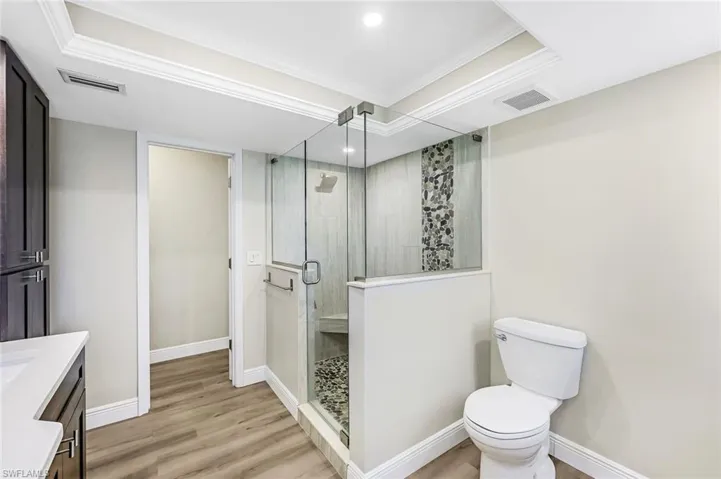 Bathroom featuring vanity, crown molding, wood-type flooring, toilet, and a shower with shower door